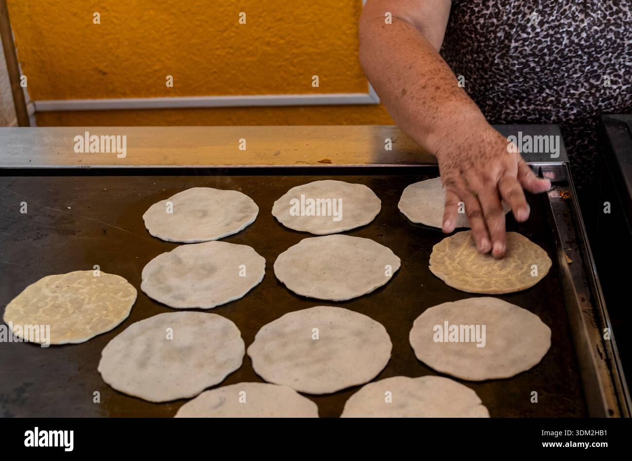 Tradizionale donna messicana che mette a mano tortillas di mais fresche sulla piastra calda. Autentica cucina comal. Foto Stock