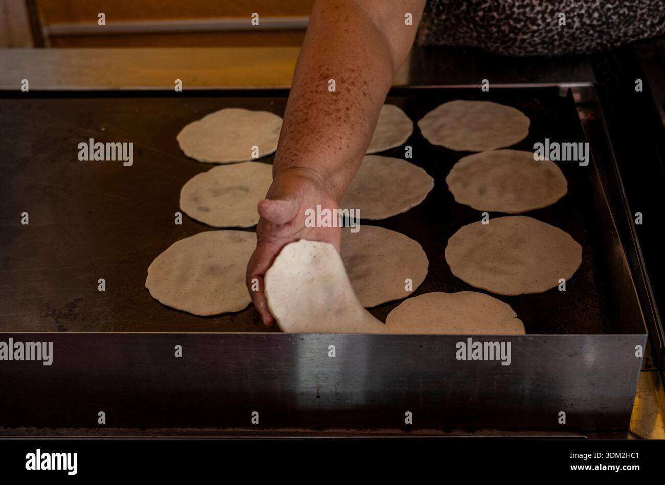 Tradizionale donna messicana che mette a mano tortillas di mais fresche sulla piastra calda. Autentica cucina comal. Foto Stock