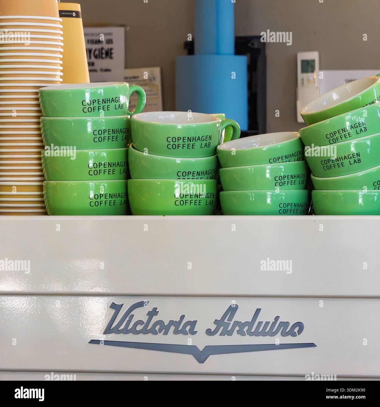Pila di tazze verdi firmate Copenhagen Coffee Lab di Victoria Arduino su un bancone di Cannes, con pipa blu e tazze gialle nel backgroun - Immagine stock catturata con smartphone