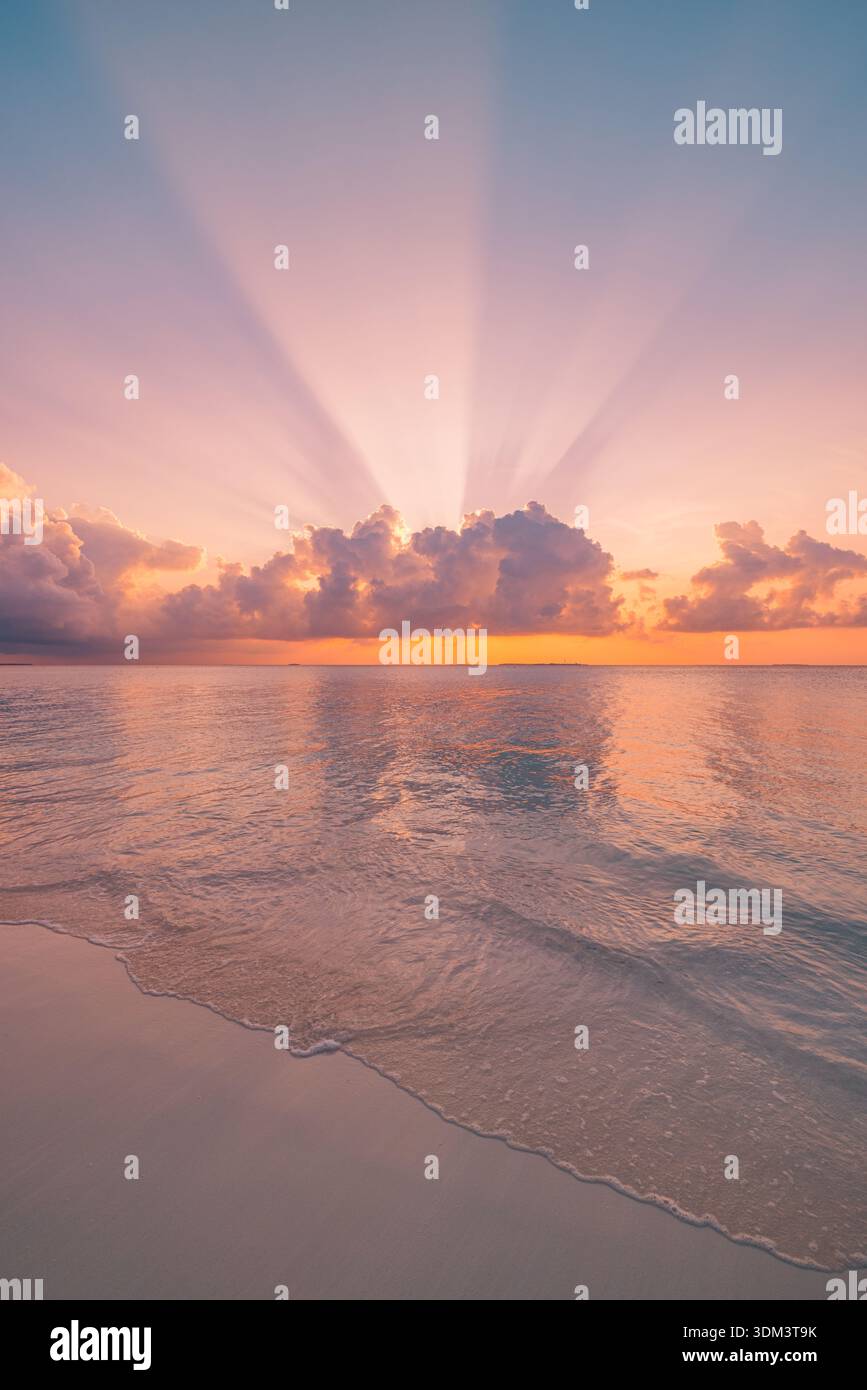 Vista mozzafiato sulla spiaggia al tramonto, con calme onde oceaniche che brillano nuvole colorate di cielo, orizzonte radioso, raggi del sole, tranquillo sfondo di viaggio estivo Foto Stock