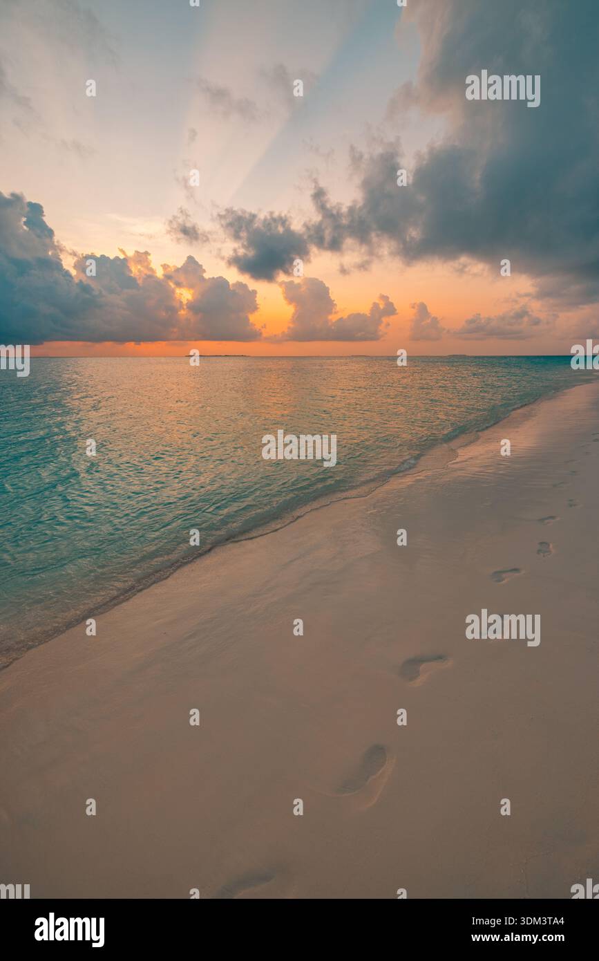 Tramonto colorato sulla tranquilla spiaggia dell'oceano con onde dolci cielo radiante nuvole all'orizzonte raggi del sole sereni d'estate ispirazione per viaggi natura Foto Stock