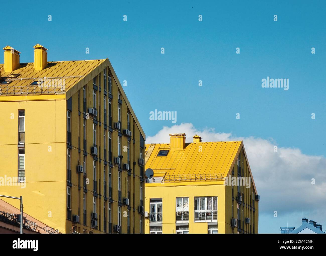 Moderni edifici di appartamenti gialli contro il cielo blu. Due case gialle di senape con tetti inclinati in un quartiere con alti edifici residenziali. Foto Stock