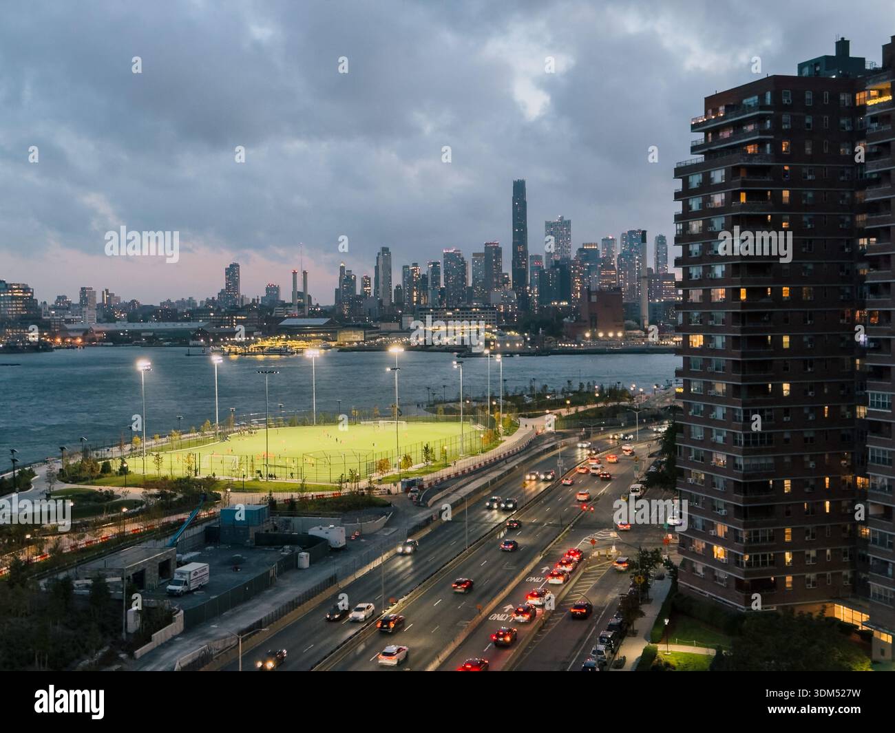 L'East River Park Field si illuminò al crepuscolo sul Lower East Side, Manhattan, con lo skyline di Downtown Brooklyn dall'altra parte dell'East River Foto Stock