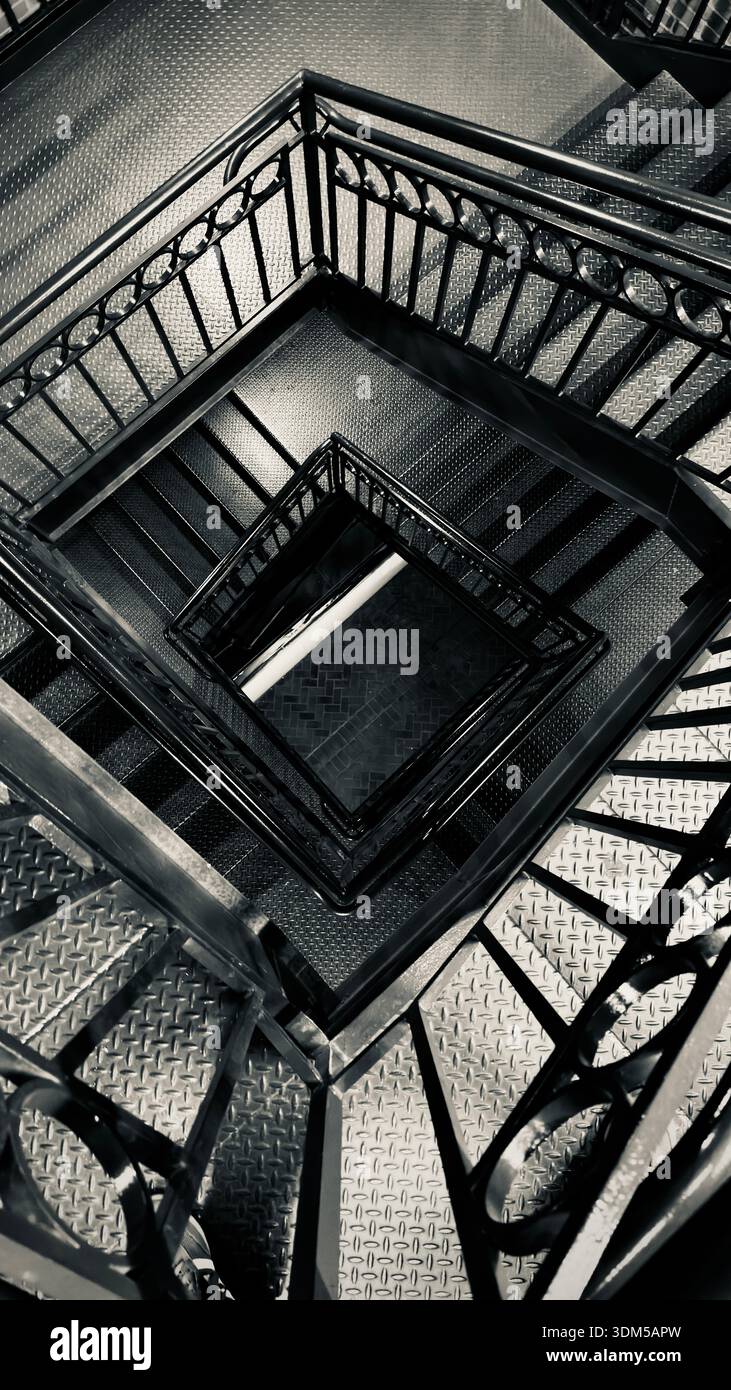 Vista dall'alto di una scala industriale in metallo con ripetizioni geometriche e forte simmetria in bianco e nero - Immagine stock catturata con smartphone