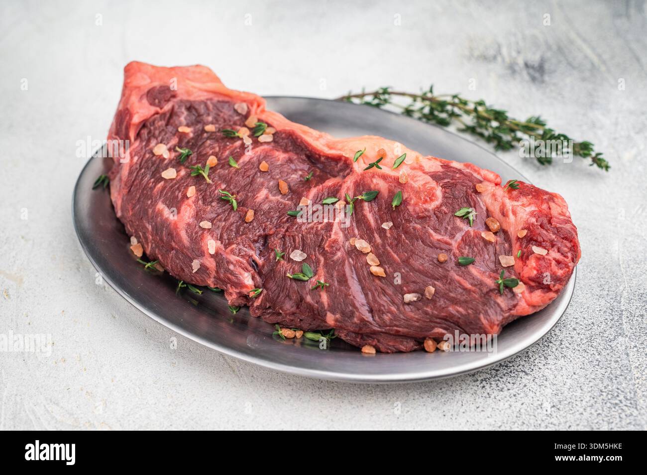 Bistecca stagionata secca con timo e sale rosa su un piatto di metallo con forchetta vintage su sfondo grigio chiaro per la cottura Foto Stock