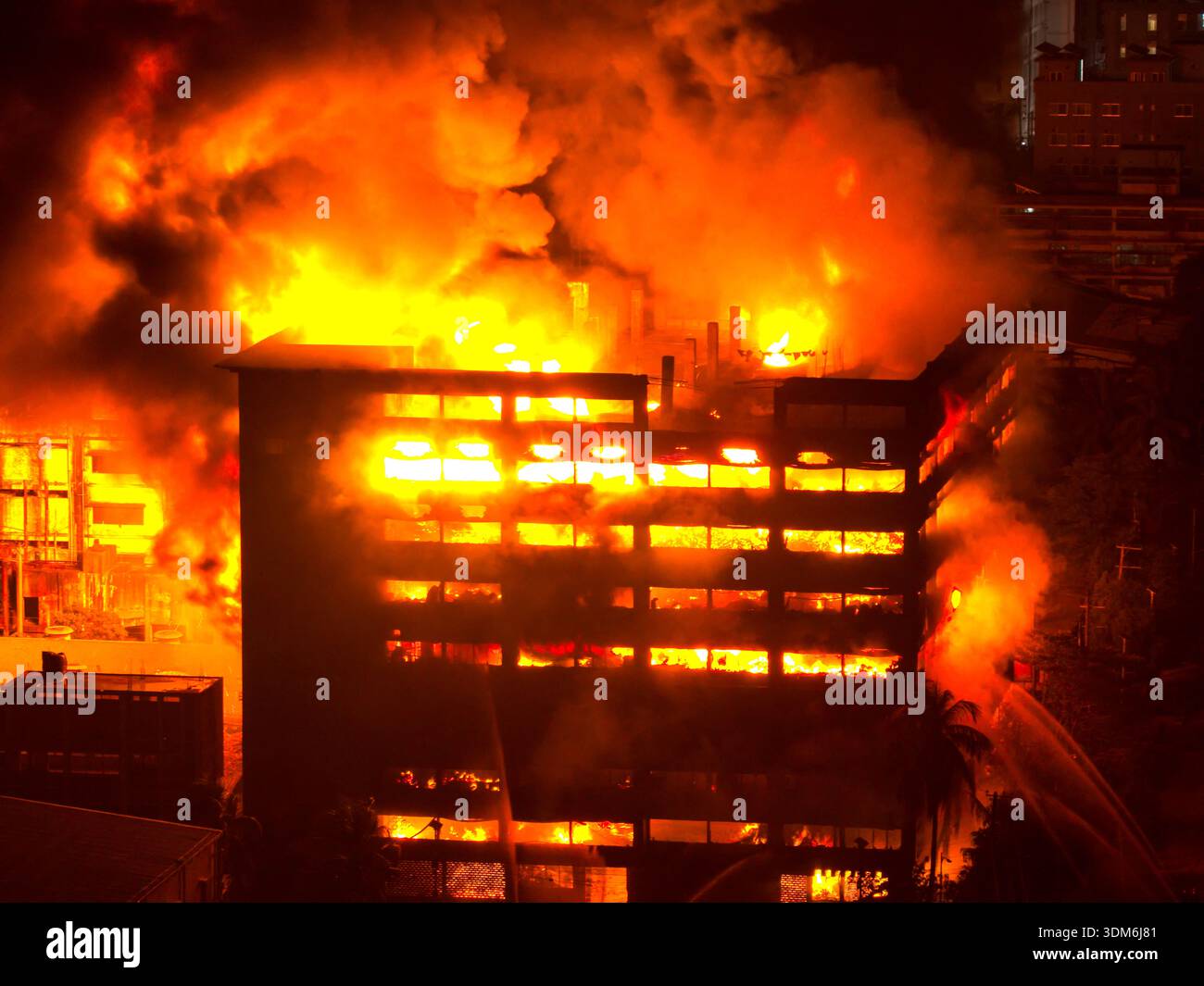Chattogram, Bangladesh - 16 ottobre 2025: Veduta aerea di un edificio inondato di fiamme, che proietta una luce arancione minacciosa contro il buio cielo notturno. Foto Stock