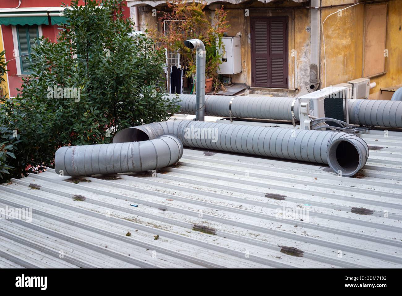 18 gennaio 2026, Roma, Italia: I tubi di ventilazione industriale e le unità di condizionamento si estendono su un tetto in metallo, contrastando l'infrastruttura urbana grezza Foto Stock
