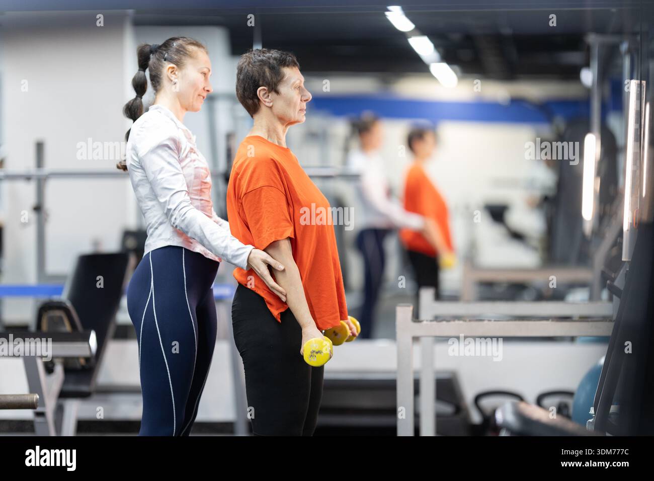 Personal trainer che guida la donna anziana che solleva i manubri Foto Stock