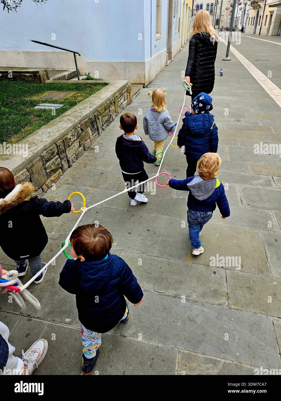 Gruppo di bambini dell'asilo che camminano con l'insegnante, passeggiata guidata sicura attraverso le strade di Capodistria, vita quotidiana nella Slovenia costiera, educazione all'aria condizionata all'aperto Foto Stock