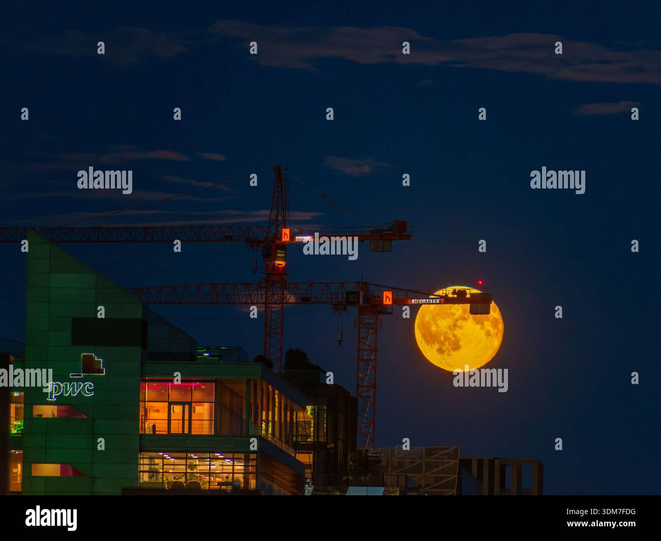 Luna che si innalza verso le gru costruendo altri appartamenti nel George's Dock di Dublino Foto Stock