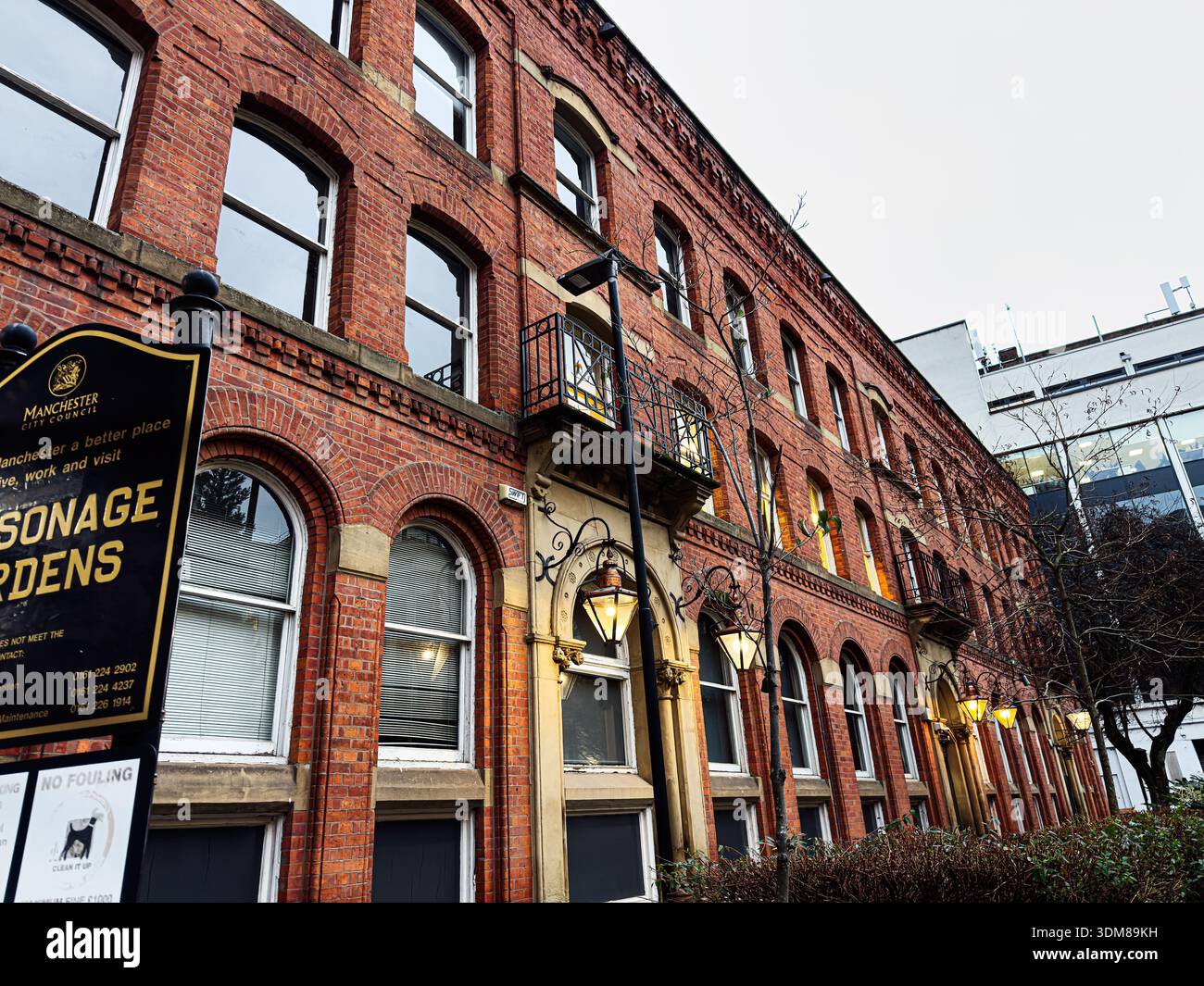 Manchester, Regno Unito - 21 gennaio 2026: Fila di case a schiera di mattoni rossi con finestre ad arco e classici lampioni stradali a Manchester, Regno Unito. Foto Stock