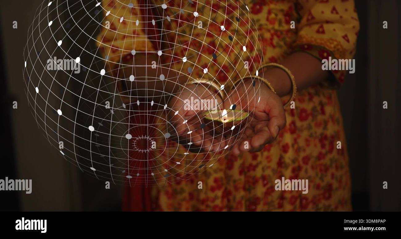 Donna indiana matura che coppetta diya di argilla illuminata in una stanza soffusa, kurta giallo, braccialetti dorati, struttura a reticolo Foto Stock