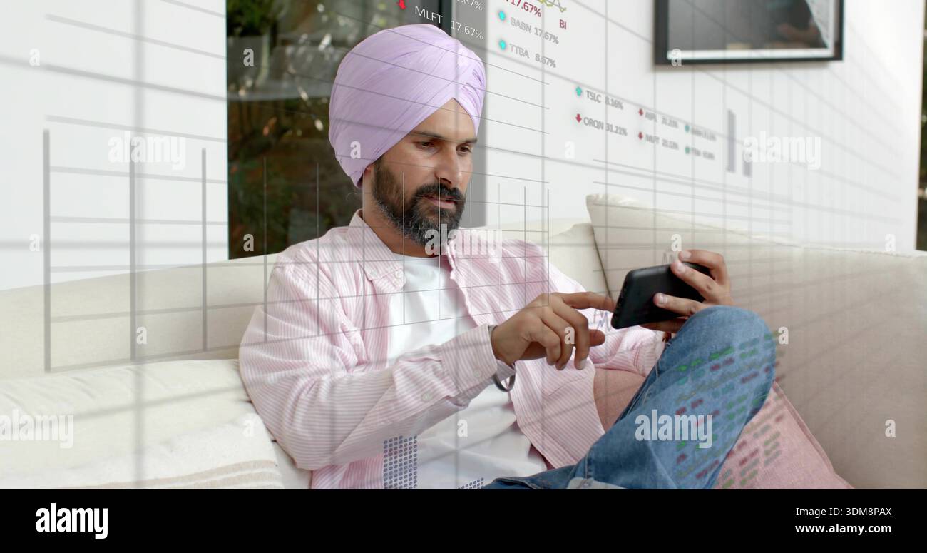 Toccare l'uomo indiano con il turbante rosa e la camicia rosa sul divano, utilizzando lo smartphone con sovrapposizioni finanziarie Foto Stock