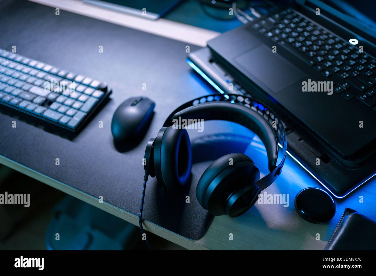 Installazione di attrezzature per videogame moderne con laptop, mouse wireless, tastiera e cuffie sul desktop sotto una luce blu fredda Foto Stock