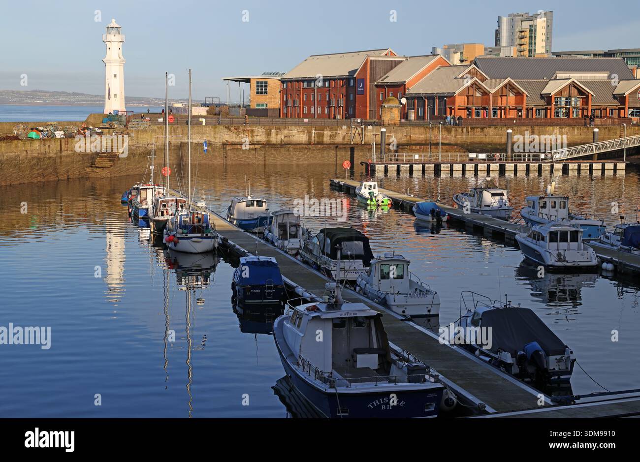Newhaven Harbour in inverno con barche da pesca e navi ormeggiate durante l'alta marea, con il faro bianco a Pier Place, Edimburgo, Scozia, Regno Unito Foto Stock