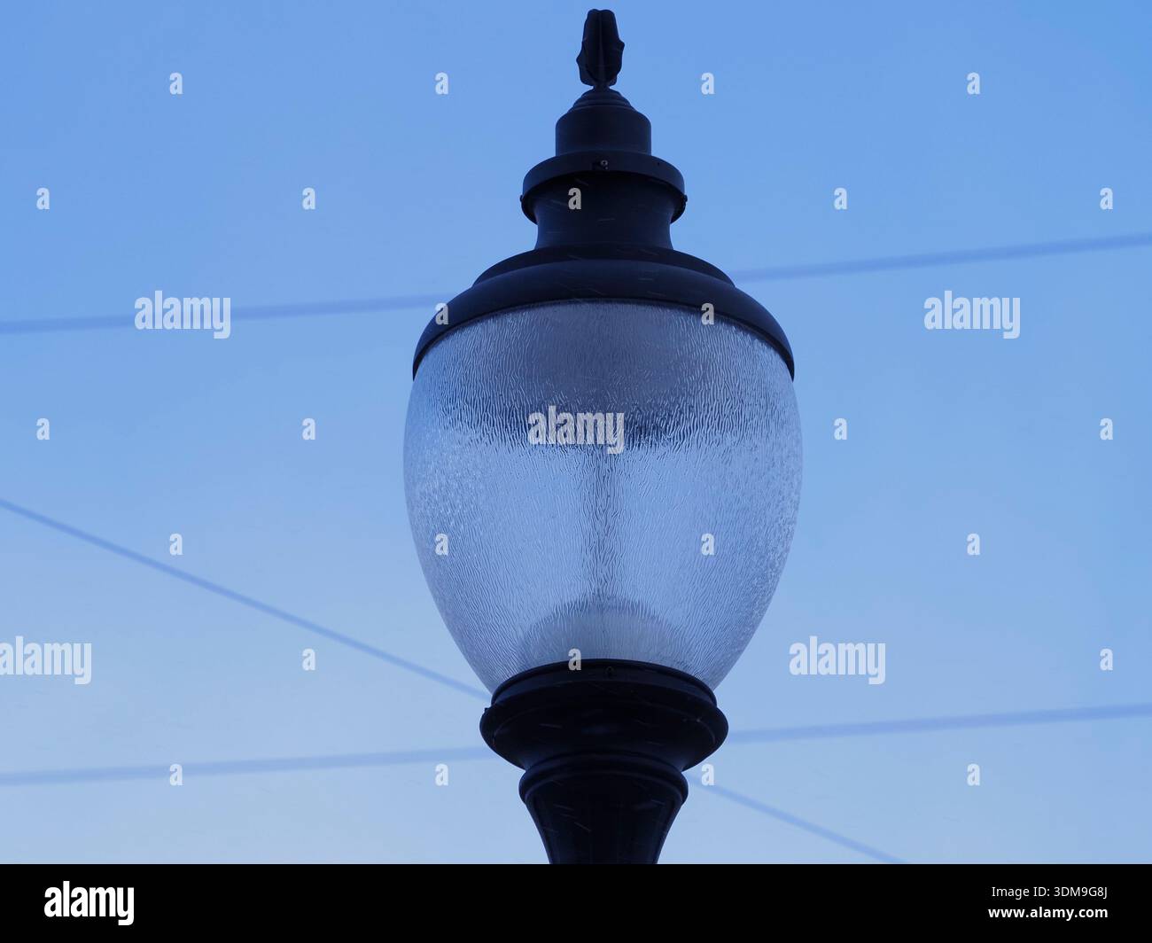 Classica lampada a lampione nera con vetro testurizzato su un cielo azzurro limpido e sottili linee aeree, composizione urbana minimalista. Foto Stock