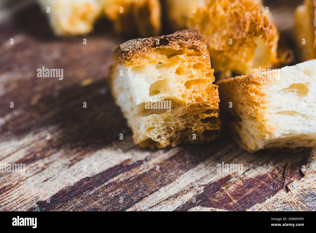 Piccoli pezzi di pane sono disposti su una superficie di legno. I pezzi mostrano tagli irregolari e cambiamenti di colore. Questa scena è probabilmente parte di un professionista della cucina o della cottura Foto Stock