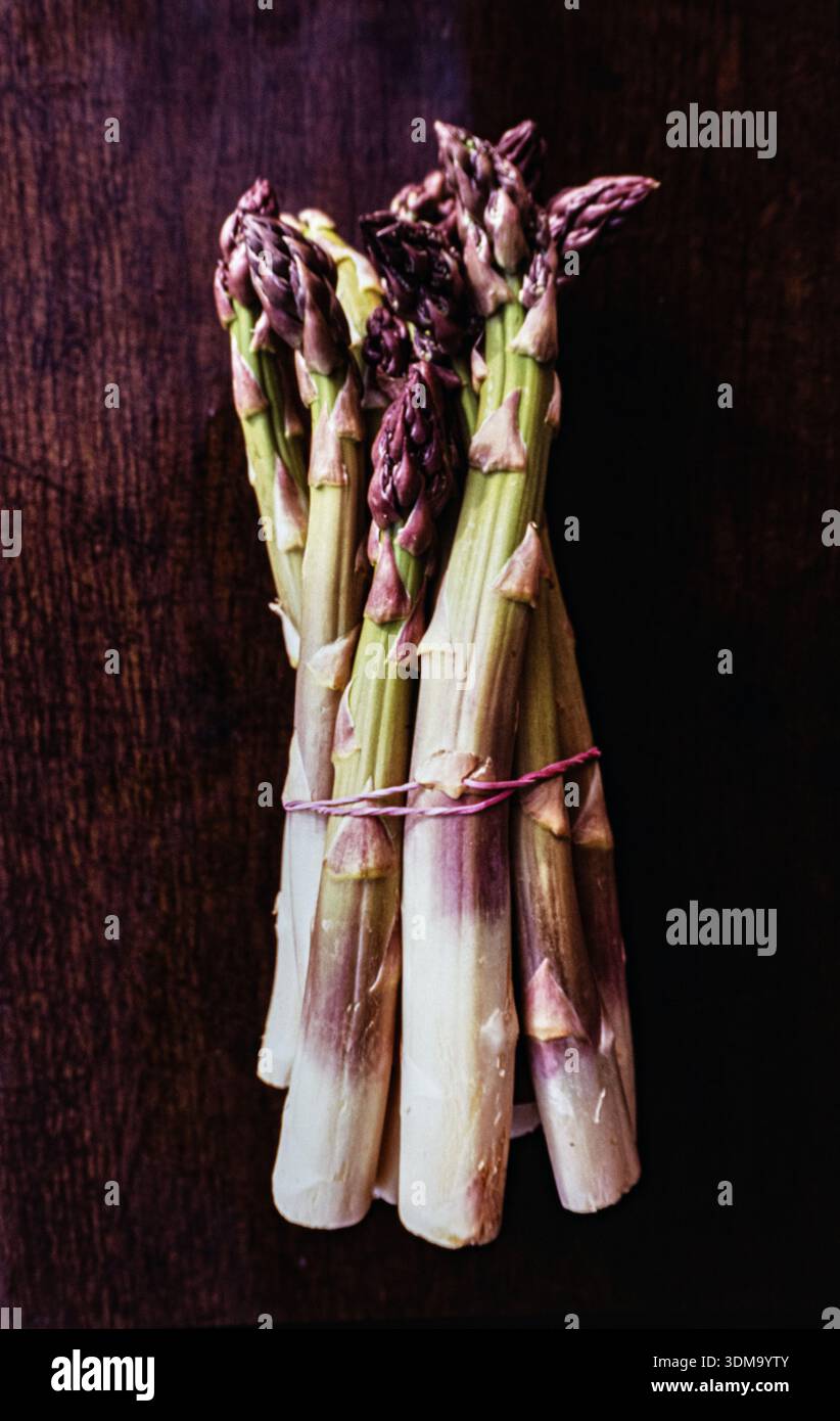 Asparagi verdi impaccati legati mostrati su una superficie ruvida in legno scuro. Vista dall'alto, disposizione piatta Foto Stock