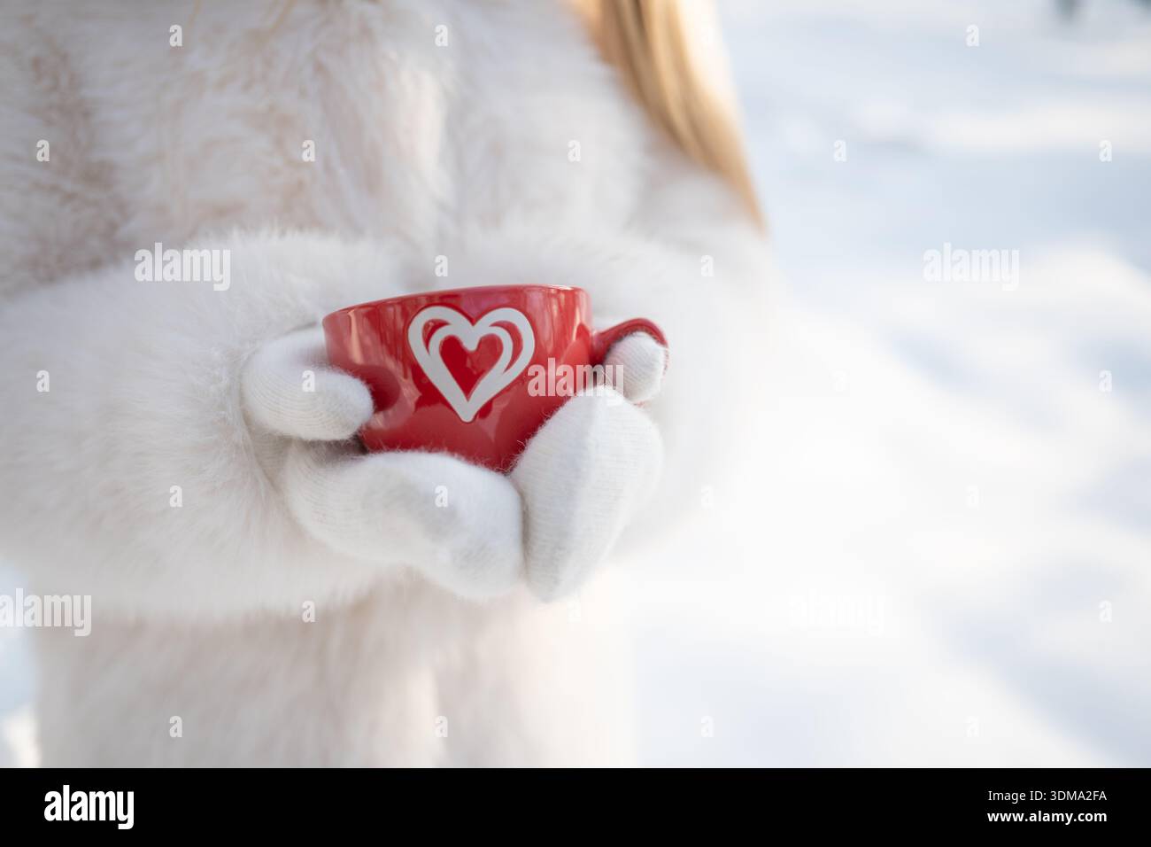 Primo piano di una tazza rossa con una bevanda calda in mani di donna all'aperto, in un ambiente invernale innevato. Foto Stock