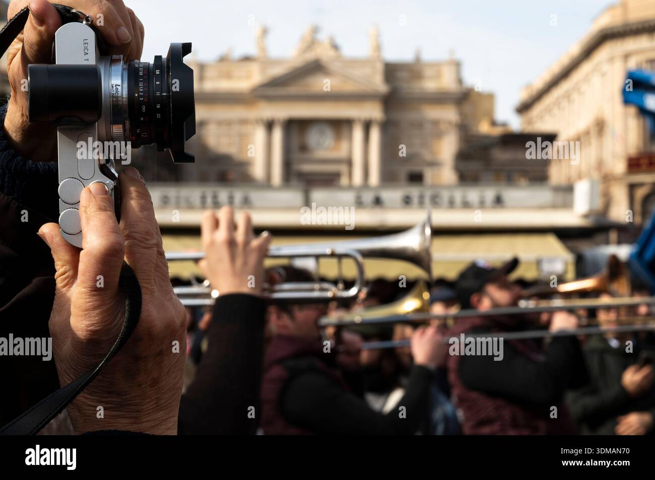 Una persona fotografa e sullo sfondo un gruppo di ottoni che eseguono e puntano i loro strumenti nella stessa direzione in Piazza Stesicor Foto Stock