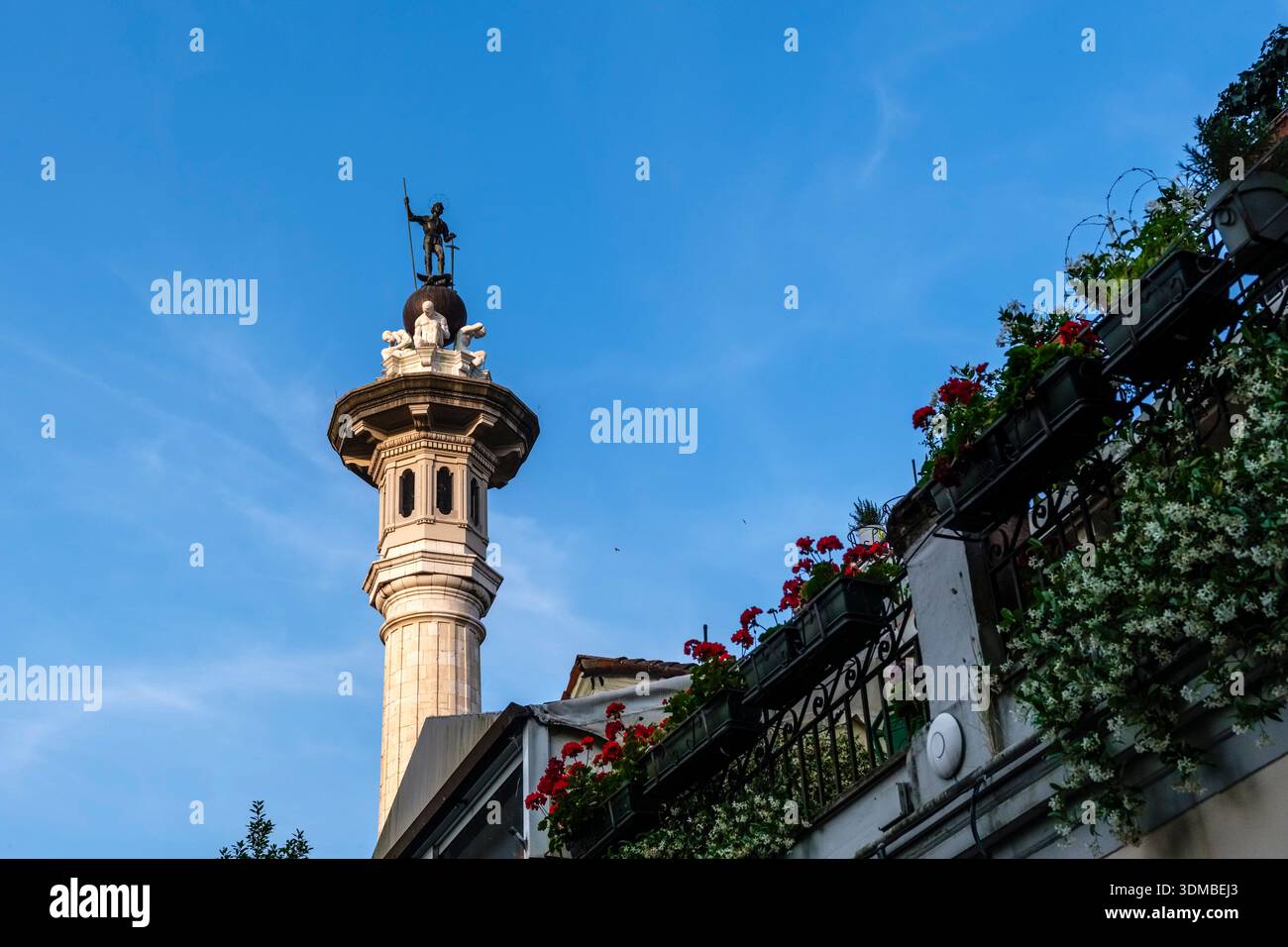 Torre neoclassica della Chiesa di San Giorgio con una statua in cima, vista dietro un balcone con fiori sotto un cielo blu. Foto Stock