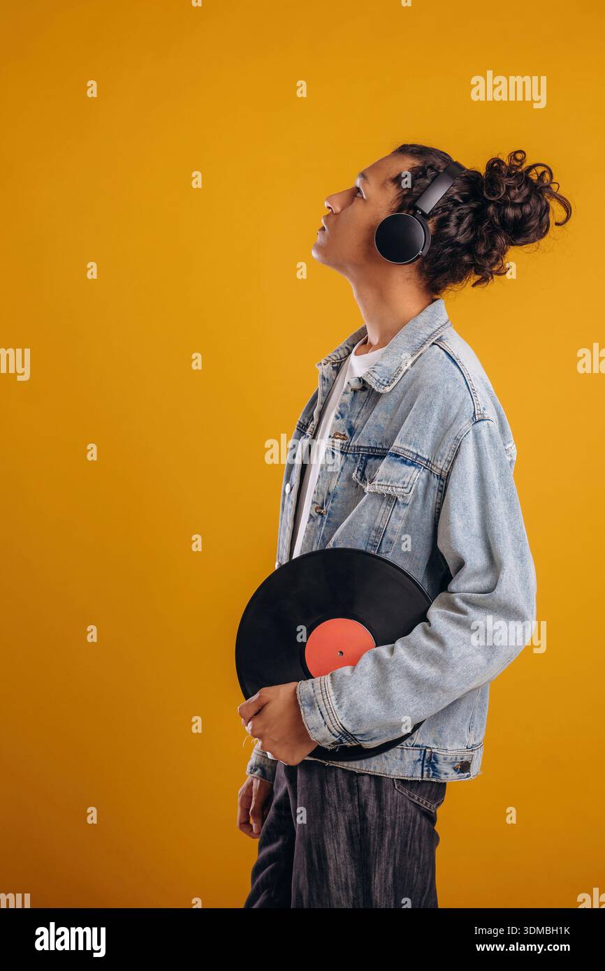 Disco in vinile retrò in mano. Il giovane ragazzo è su sfondo giallo. Foto Stock