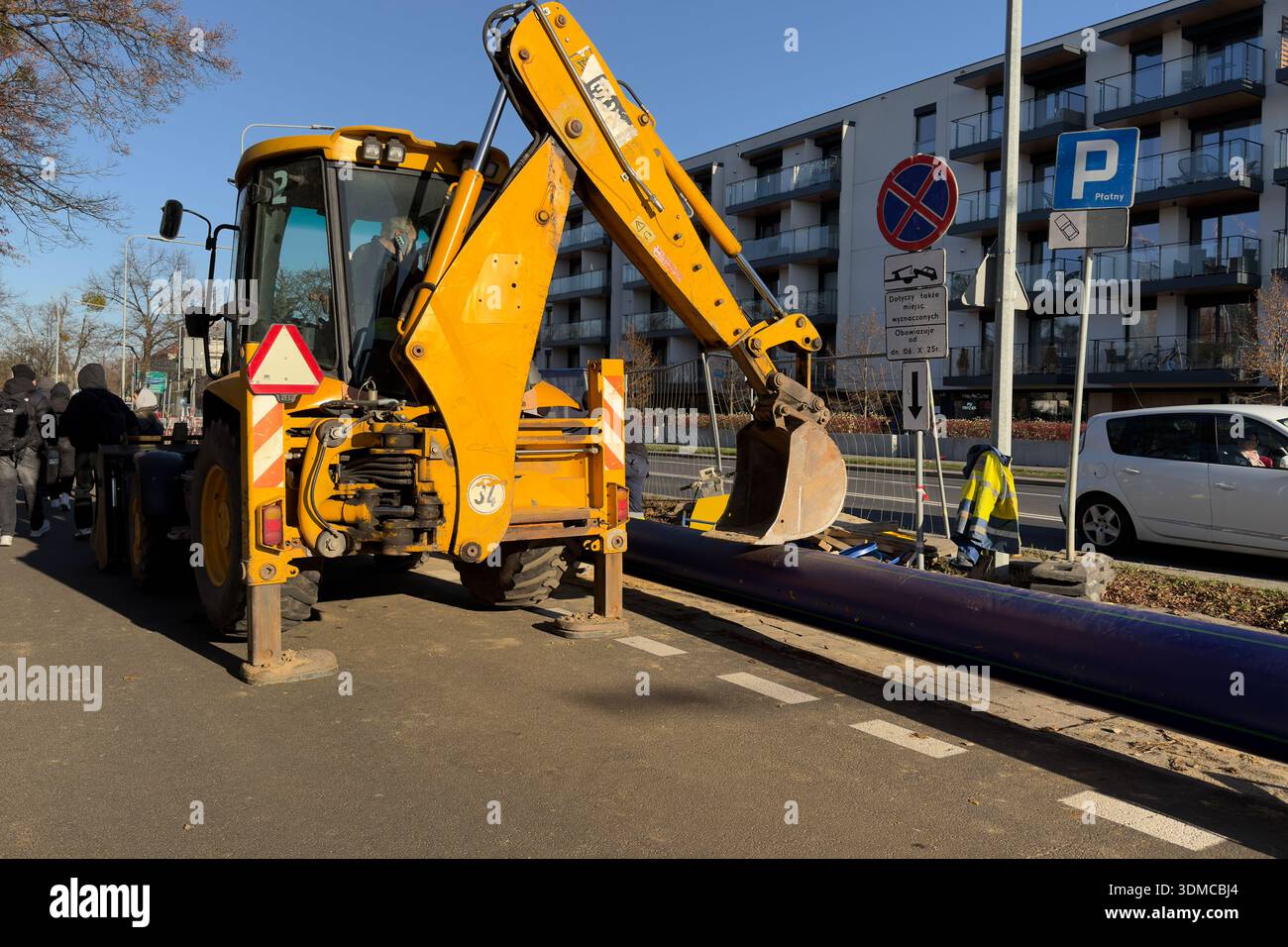 Poznan, Polonia - 18 novembre 2025: Terna gialla con pala vicino alla conduttura viola, che mostra i lavori di ingegneria civile e lo sviluppo di servizi urbani vitali Foto Stock