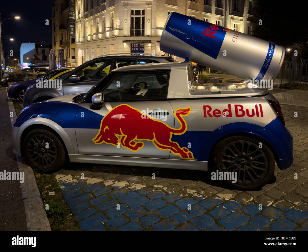 Poznan, Polonia - 18 novembre 2025: La speciale Mini Cooper di Red Bull, con un'enorme replica di lattine, cattura gli occhi sulla strada della città di notte, aumentando il presen del marchio Foto Stock