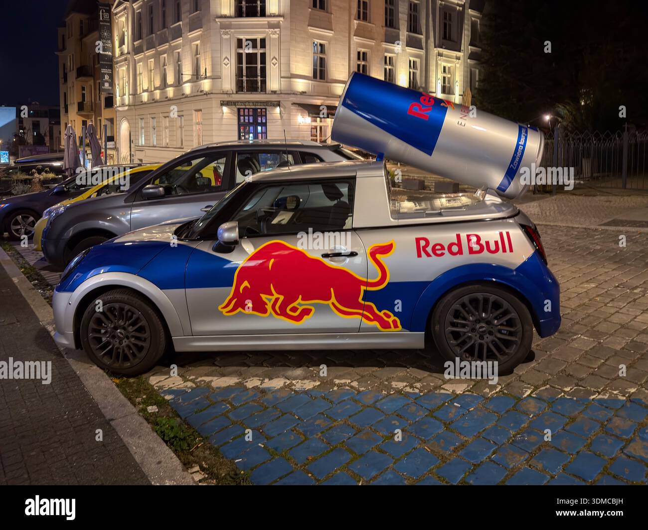Poznan, Polonia - 18 novembre 2025: Veicolo Red Bull Mini Cooper con bomboletta di energia gigante, parcheggiato su strade urbane di notte, per un'efficace promozione del marchio Foto Stock