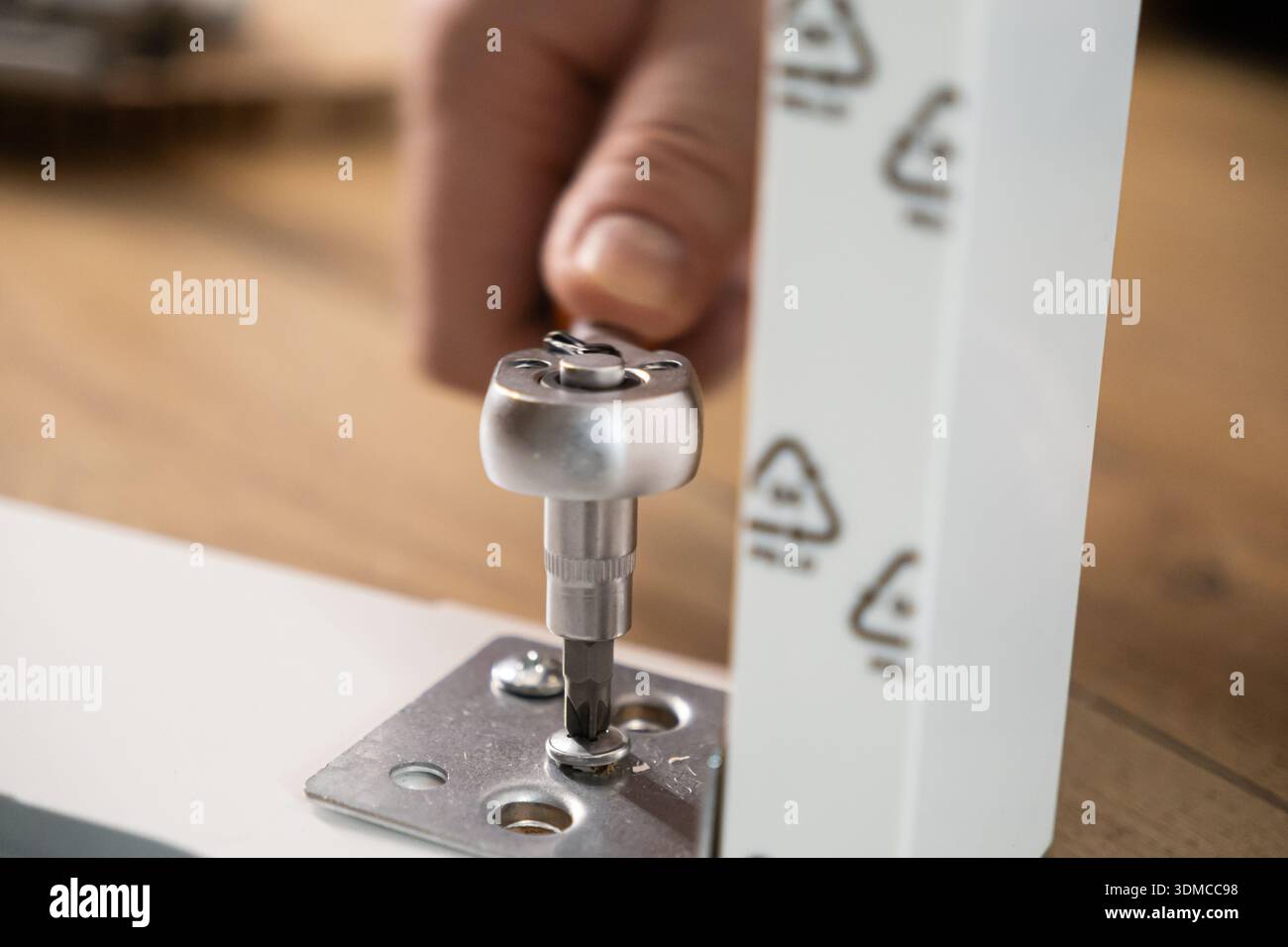 L'immagine di dettaglio mostra un singolo mobile bianco assemblato, utilizzando con cautela un cacciavite a cricchetto argentato per fissare una vite a un componente metallico, riflessi Foto Stock