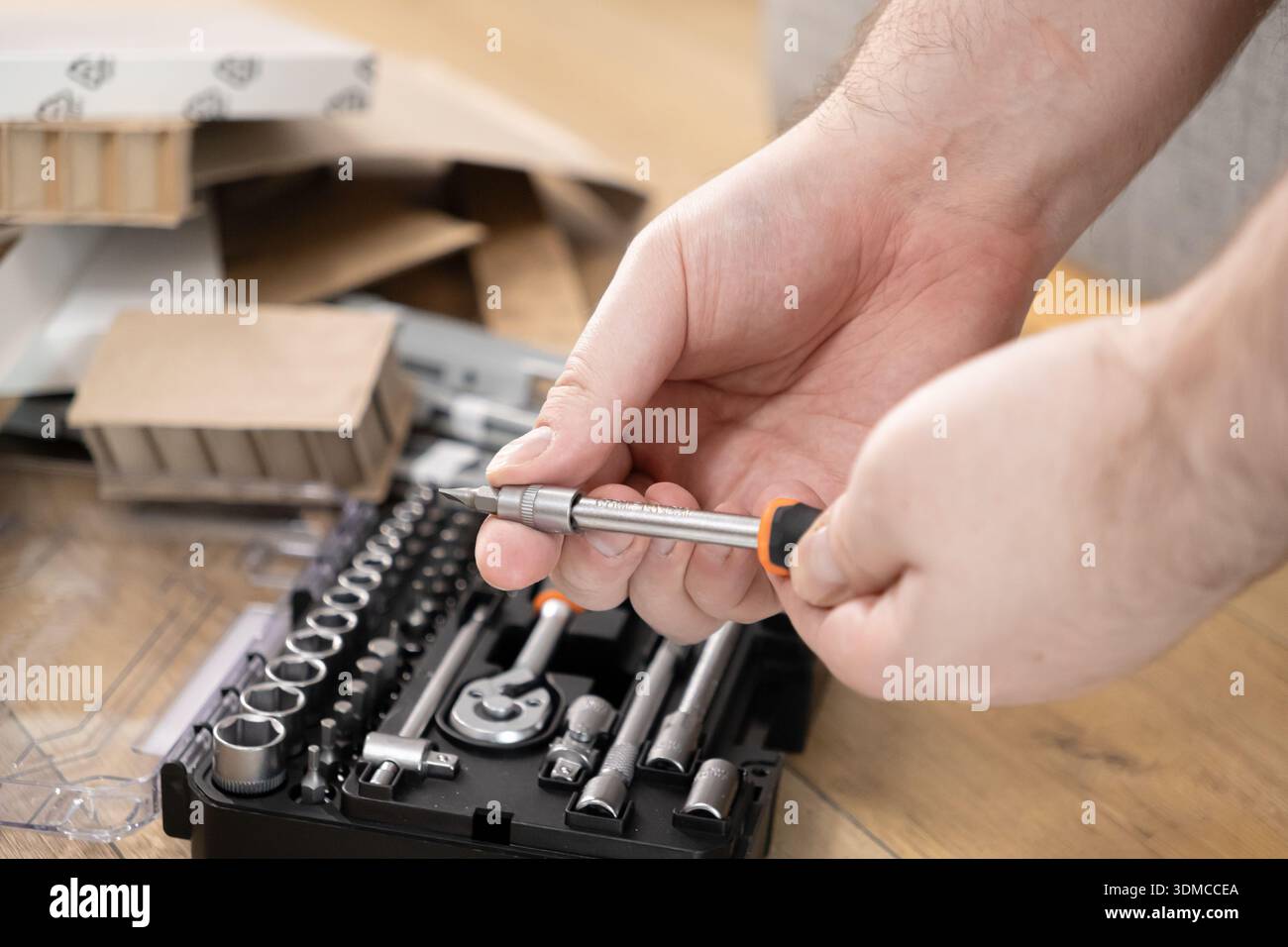 Primo piano di mani che selezionano una punta per cacciavite di precisione da un kit di utensili completo, preparandosi per l'assemblaggio di mobili fai da te e per le attività di riparazione domestica Foto Stock