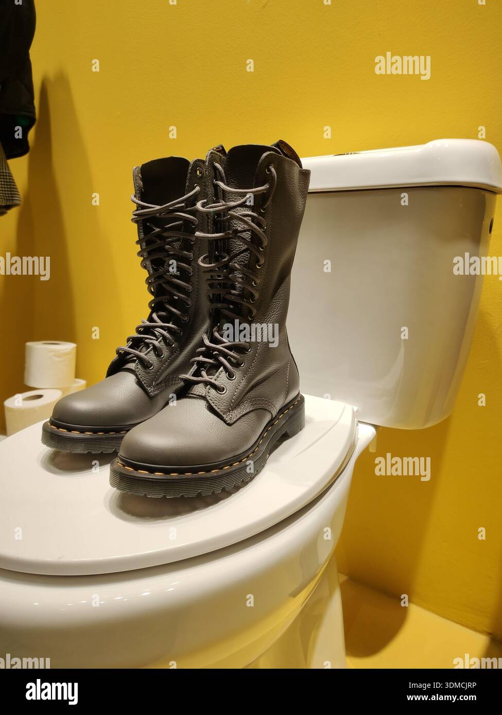 Dettaglio di stivali in pelle nera con lacci esposti su una ciotola con sfondo giallo nella vetrina di un negozio di abbigliamento e moda Foto Stock