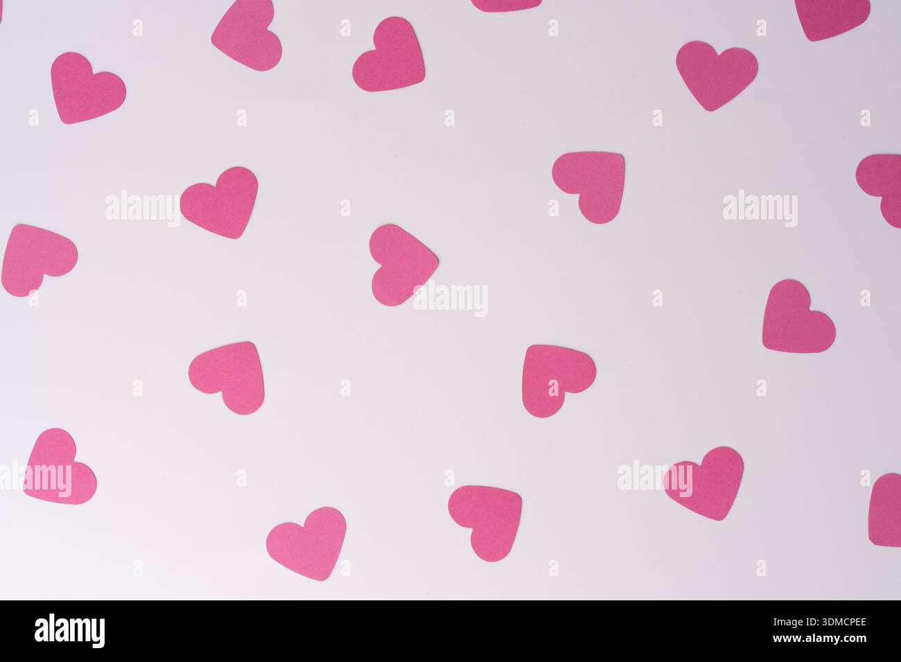 Una giocosa disposizione di piccoli cuori di carta rosa su una superficie bianca pulita, che evocano sentimenti di amore, celebrazione e gioia. Foto Stock