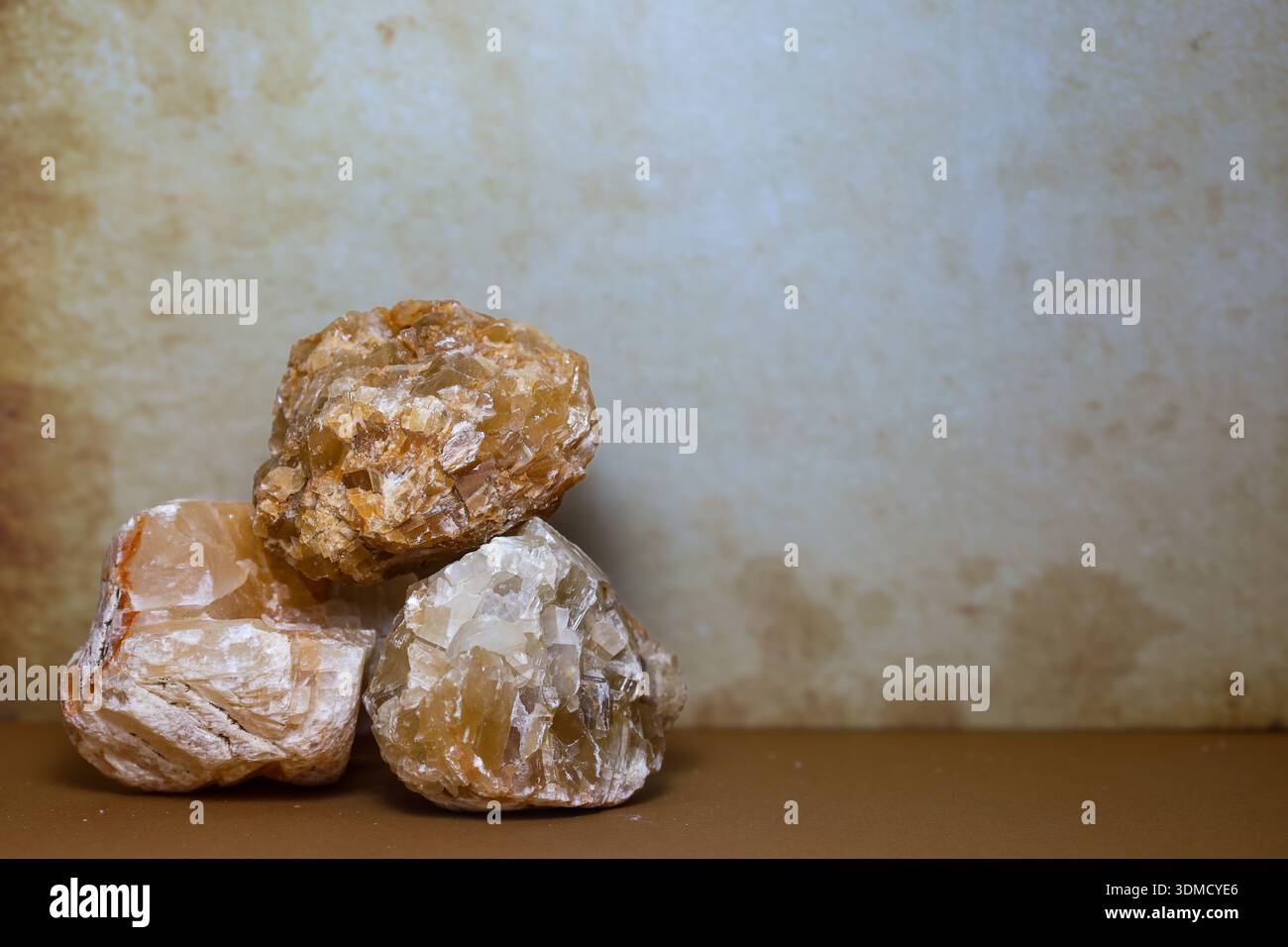 Tre cristalli di calcite di miele grezzo disposti in una struttura piramidale stabile su una superficie neutra. Foto Stock