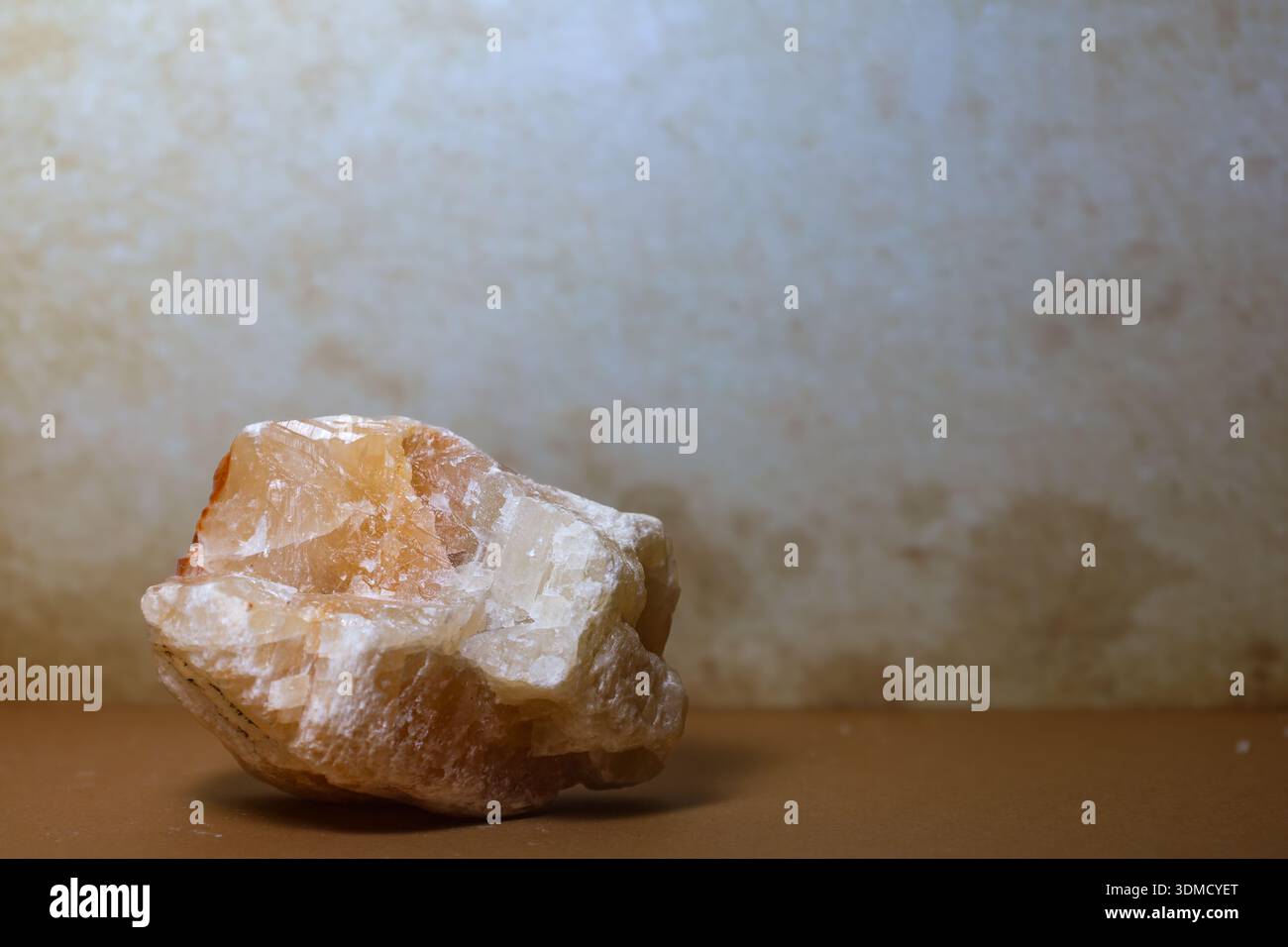 Descrizione: Una singola pietra di calcite a base di miele crudo posta su una superficie dai toni caldi e con sfondo testurizzato. Foto Stock
