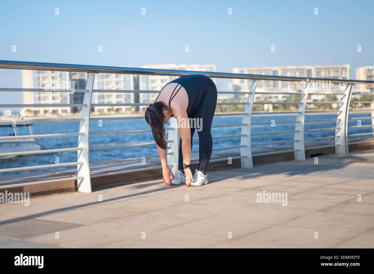 Una donna incinta esegue un esercizio di stretching sul lungomare, dimostrando il suo impegno per il fitness in un ambiente sereno che incoraggia un'attività fisica Foto Stock