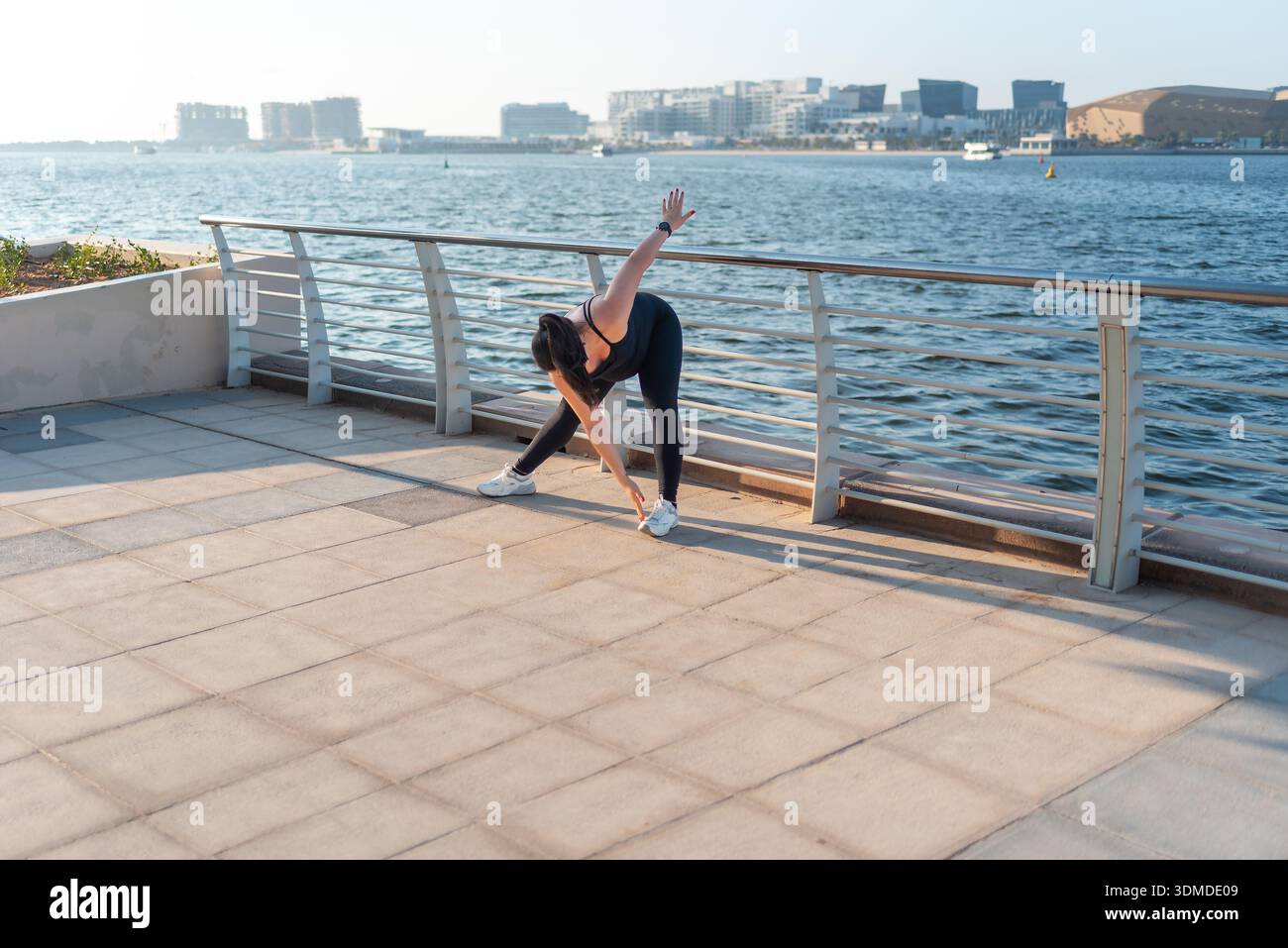 Una donna incinta esegue un esercizio di stretching sul lungomare, dimostrando il suo impegno per il fitness in un ambiente sereno che incoraggia un'attività fisica Foto Stock