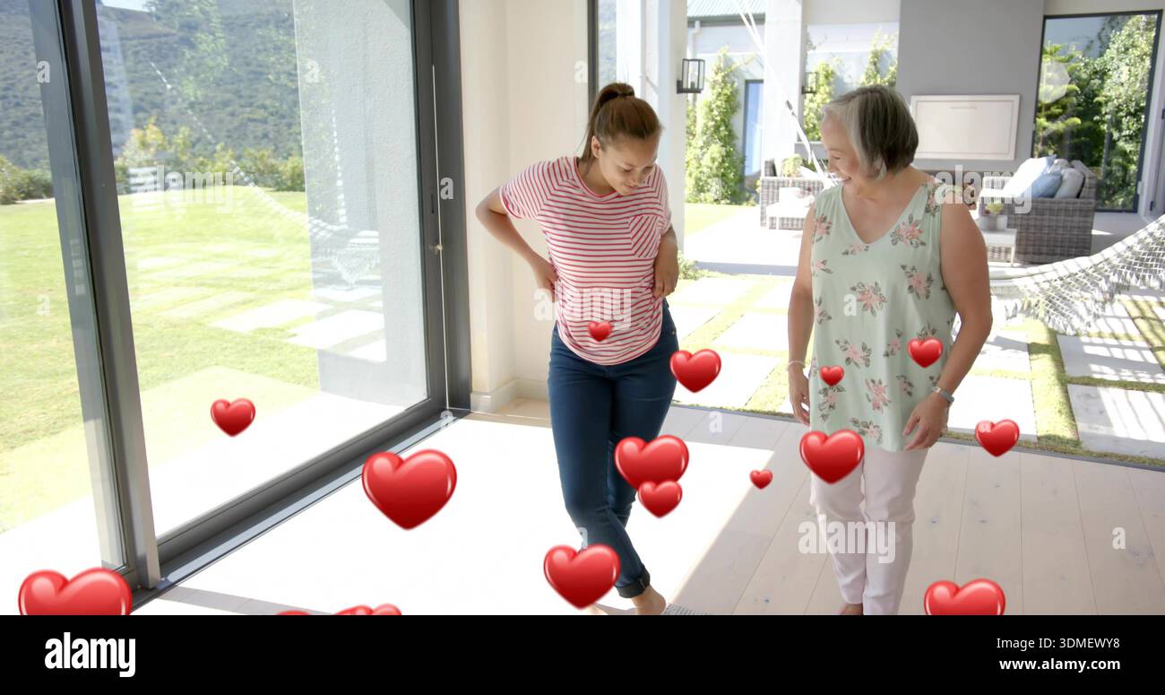 Donna sorridente con top floreale che abbraccia adolescente con top a righe vicino a porte scorrevoli in vetro, con cuore Foto Stock