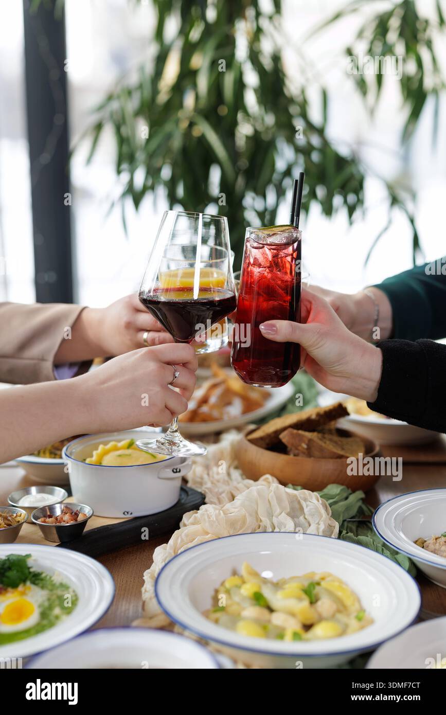 Durante il pasto condiviso, il gruppo sorseggia vino, cocktail e bicchiere di succo di frutta. Ideale per l'ospitalità, lo stile di vita sociale e le campagne di marketing di celebrazione. Foto Stock