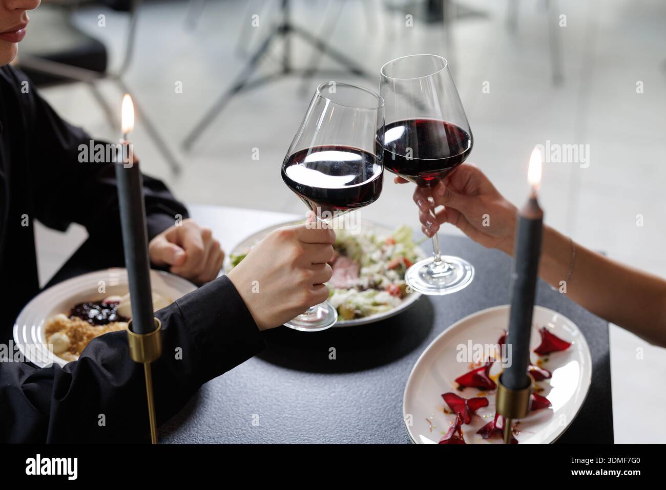 Coppia che sorseggia bicchieri di vino rosso durante una cena intima a lume di candela. Adatto per stile di vita, incontri, ospitalità e grafica di marketing di celebrazione Foto Stock