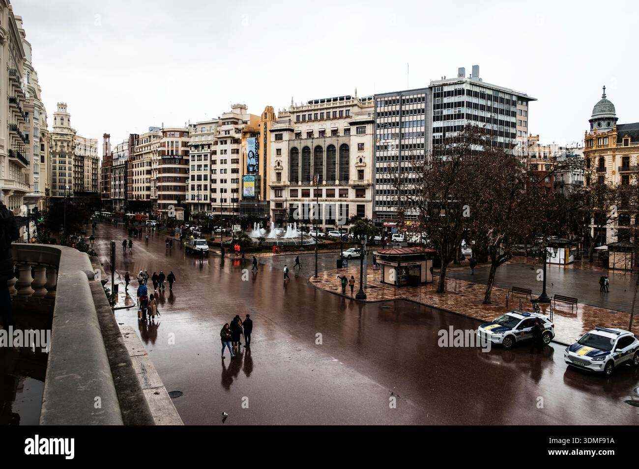 Vista elevata di una piazza della città piovosa a Valencia, Spagna, caratterizzata da un'architettura storica, una fontana e la vita urbana di strada. Foto Stock