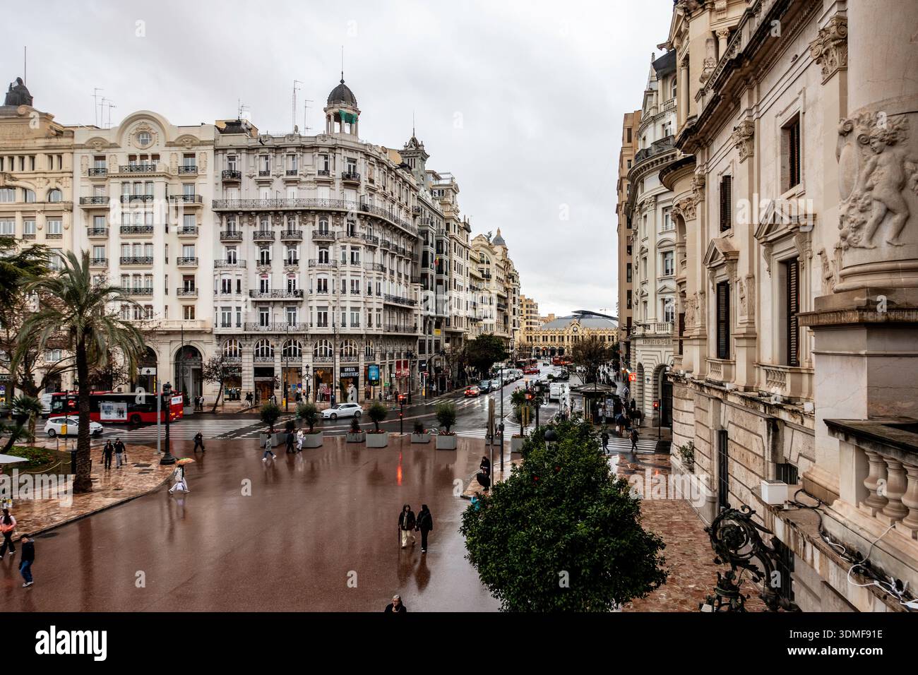 Storica scena di strada europea a Valencia, Spagna, con grandi edifici neoclassici e strade acciottolate bagnate sotto un cielo nuvoloso. Foto Stock