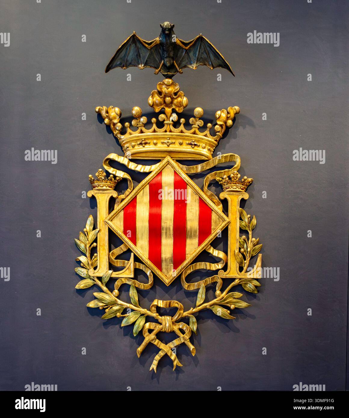 Uno stemma decorato placcato oro di Valencia, Spagna, con l'iconico pistrello e corona, esposto su una parete scura all'interno dello storico municipio. Foto Stock