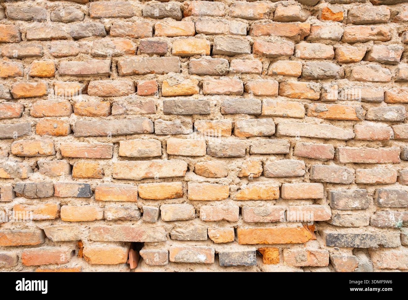 Una parete in mattoni rustici mostra mattoni arancioni, abbronzati e grigi con superfici ruvide. Ideale per progetti di architettura, design o urban mood alla ricerca di Foto Stock