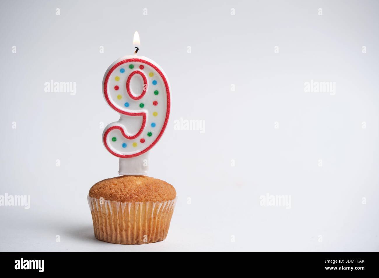Cupcake di compleanno con la candela numero 9 accesa su sfondo bianco Foto Stock