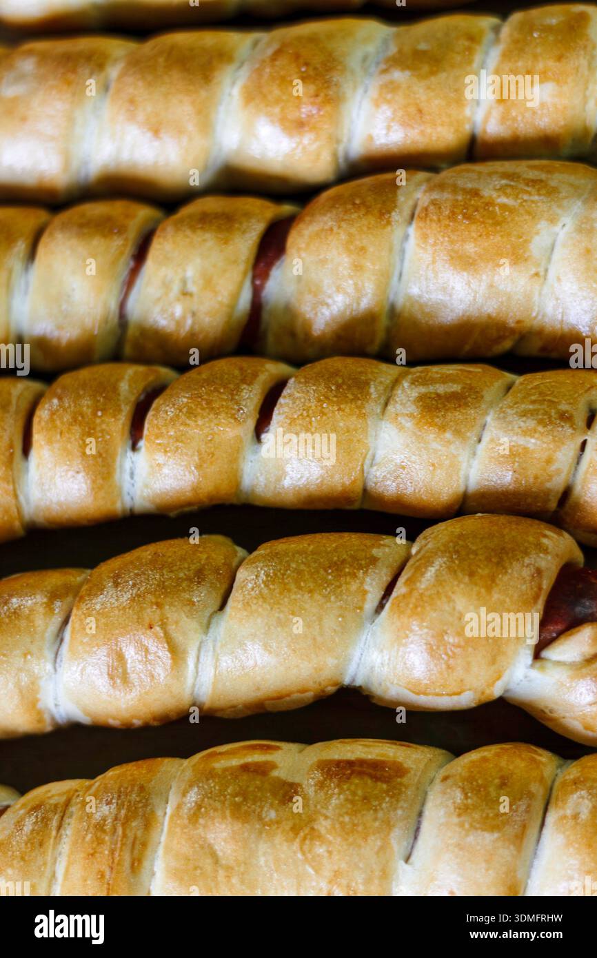 Primo piano di involtini di salsiccia dorati al forno con impasto croccante in una vetrina da forno. Foto Stock