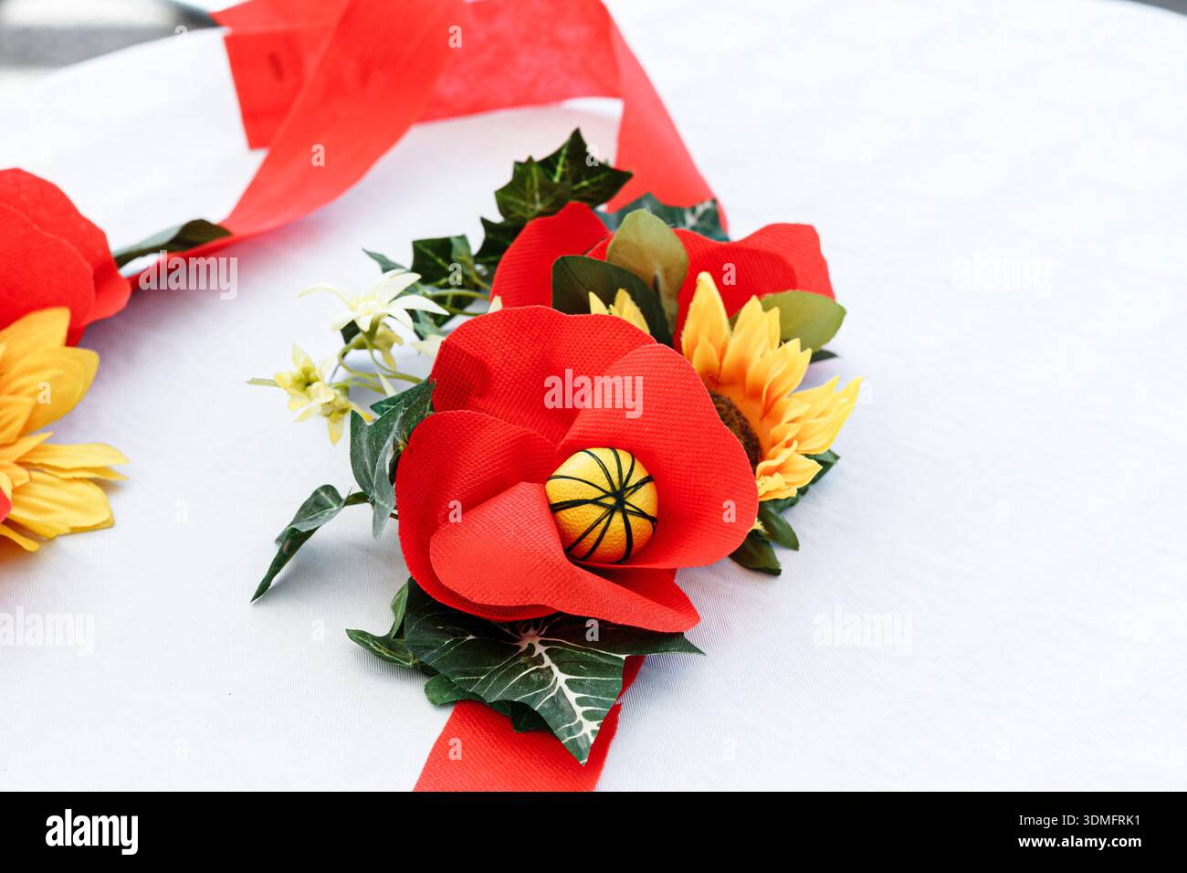 Composizione floreale artificiale con papaveri rossi e girasoli gialli su un tavolo bianco per decorazioni festive. Foto Stock