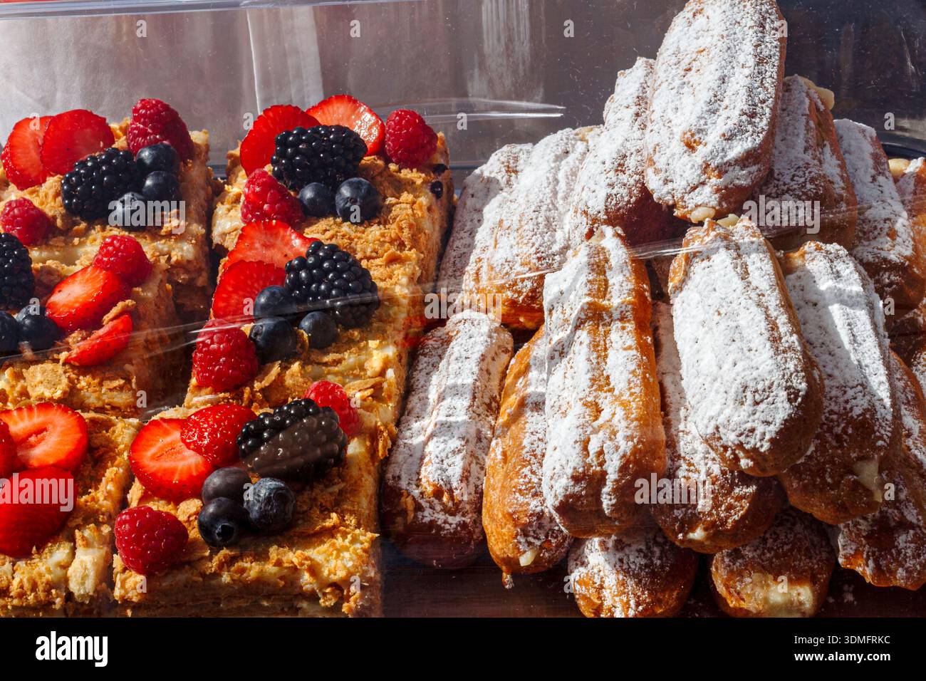 Varietà di torte, eclari e pasticcini a bacca esposti in una cassa da forno professionale per i clienti. Foto Stock