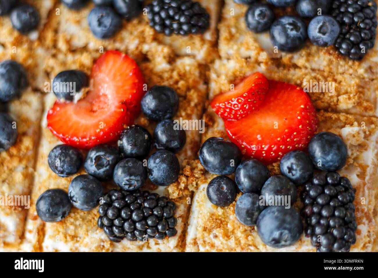 Fette di torta gourmet con mirtilli neri, fragole e panna che mostrano ricchi strati di sapore. Foto Stock