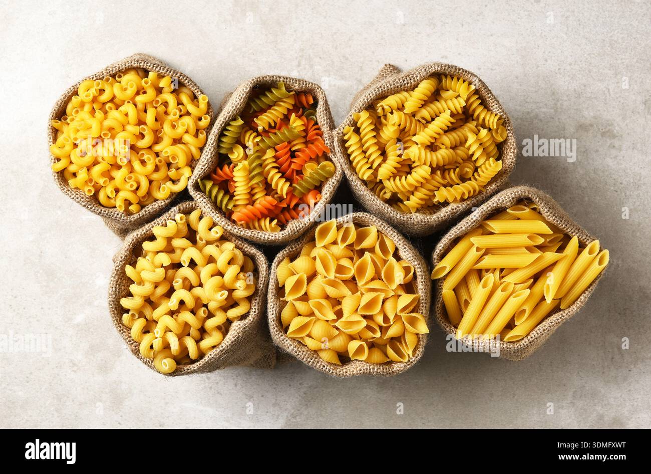 Sei sacchetti di burlap pieni di vari tipi di pasta cruda. Foto Stock